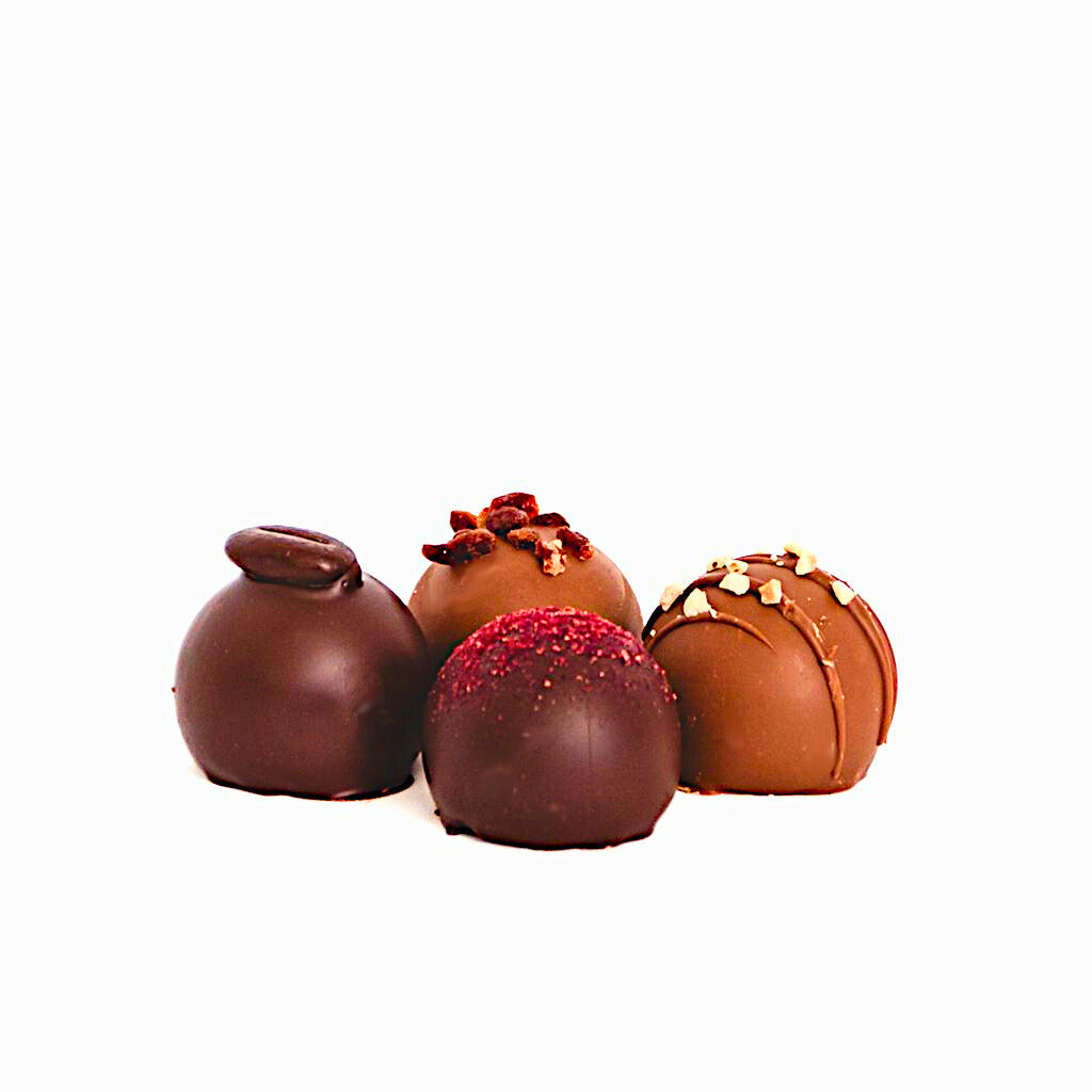 Four chocolate truffles with different toppings on a white background