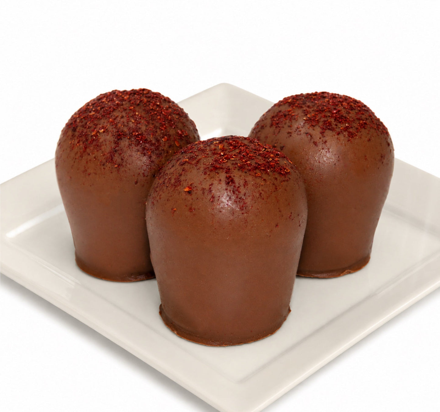 Three chocolate truffles with a powdered blackberry topping on a white plate.