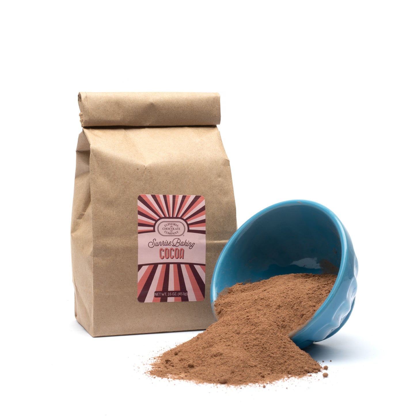 A brown paper bag of Euphoria Chocolate Company Sunrise Baking Cocoa with a blue bowl spilling cocoa powder in front of it against a white background.