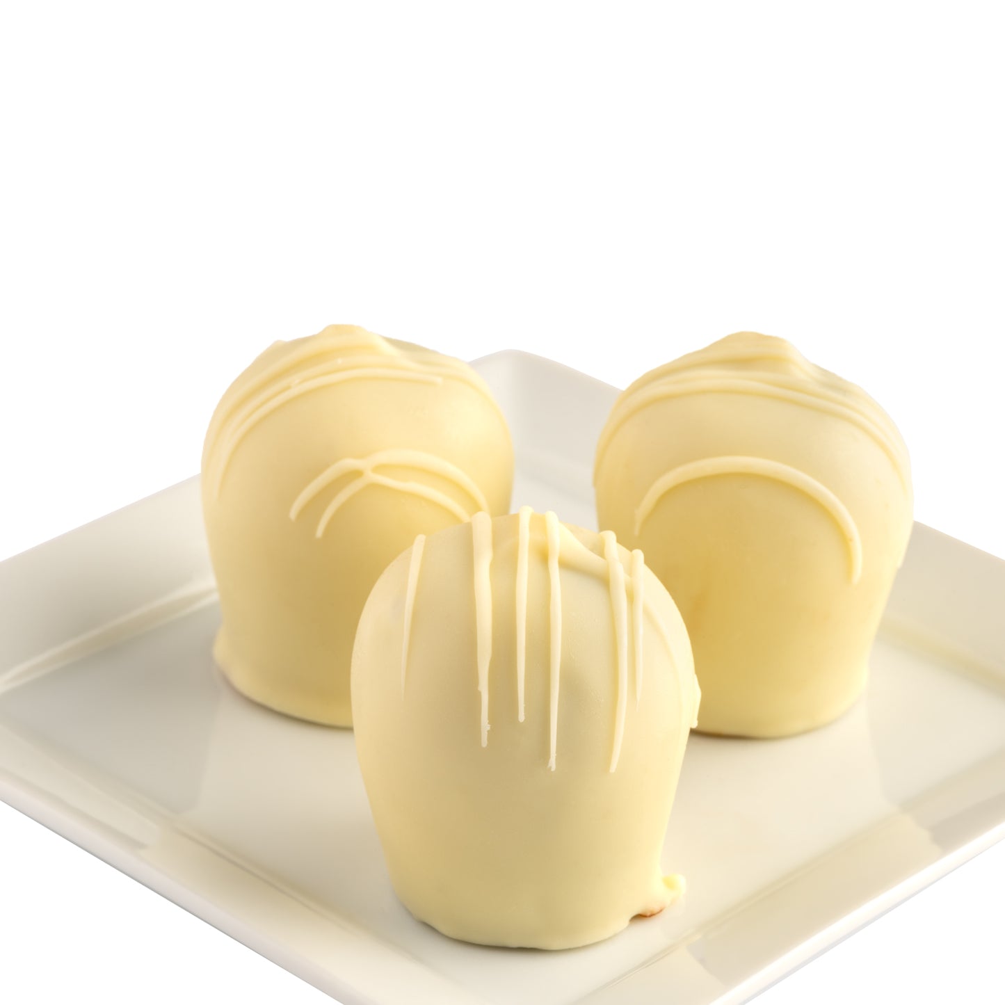 Three white chocolate truffles with white chocolate cross hatch patterns on a white plate in front of a white background.