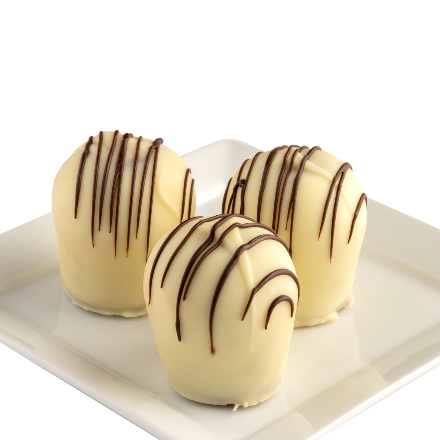 A box of three hand-dipped white chocolate truffles with dark chocolate stripes, on a white plate in front of a white background.