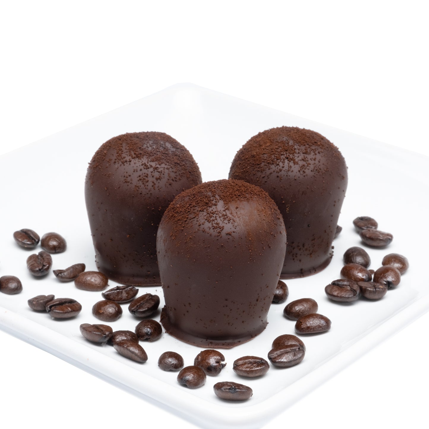 Three Midnight Kona truffles with a sprinkling of ground Hawaiian Kona coffee on top, presented with scattered coffee beans around them on a white plate against a white background.