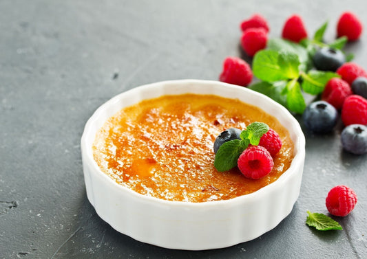 Creme brulee in a white dish with fruit.