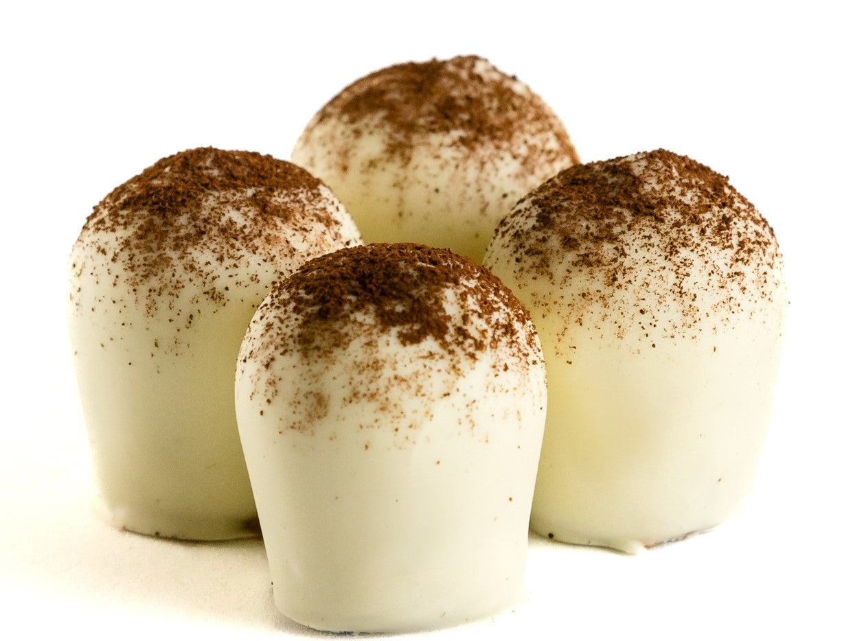 Four white chocolate truffles with cocoa powder dusting on white background