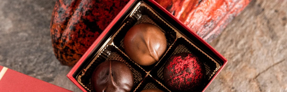 An open red gift box containing four of Euphoria Chocolate Company's Classic truffles, with two smooth milk chocolate truffles and two dark chocolate truffles with red powder, set against a rustic background.