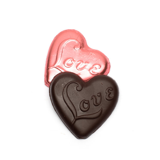 Two heart-shaped chocolates, one wrapped in pink foil and one made of dark chocolate, with 'love' engraving on a white background.