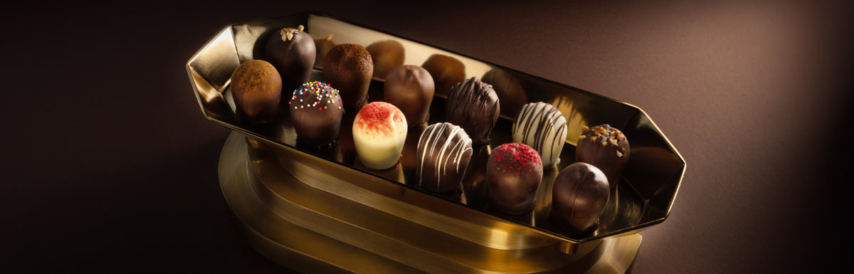 An assortment of Euphoria Chocolate Company Classic Truffles in a gold hexagonal dish, set against a dark brown background.