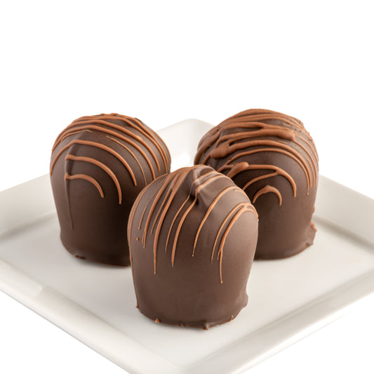 Three chocolate truffles with a stripe on a white plate with a white background