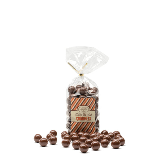 A clear plastic bag filled with milk chocolate covered caramel candies with sea salt, displayed with loose caramel candies scattered in front and labelled with the Euphoria Chocolate Company logo against a white background.