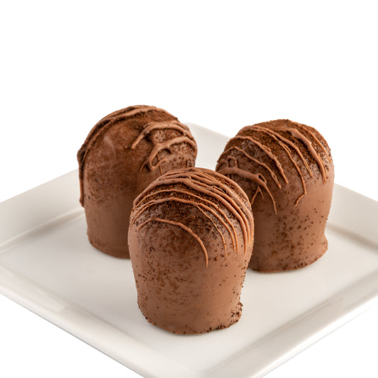 Three Euphoria Chocolate Company hazelnut latte truffles drizzled with chocolate topping and Kona coffee grounds, arranged on a white square plate against a white background.
