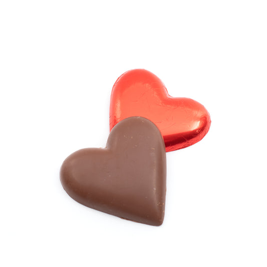 Two heart-shaped chocolates, one wrapped in red foil and one made of chocolate, on a white background