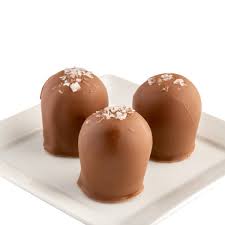 Three milk chocolate truffles topped with sea salt on a white plate with a white background