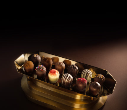 An assortment of Euphoria Chocolate Company Classic Truffles in a gold metal tray, set against a dark brown background with dramatic lighting.