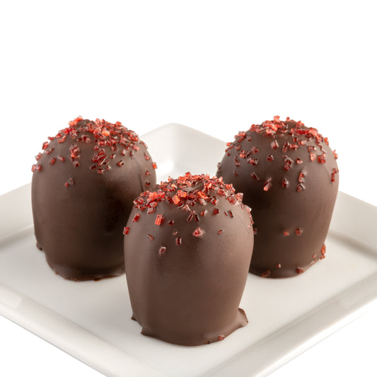 Three dark chocolate truffles with red flavor sprinkles on a white plate