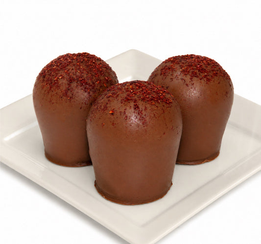 Three chocolate truffles with a powdered blackberry topping on a white plate.