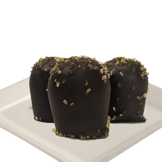 Three dark chocolate truffles with passionfruit flavor, garnished with gold flakes, on a white plate and a white background