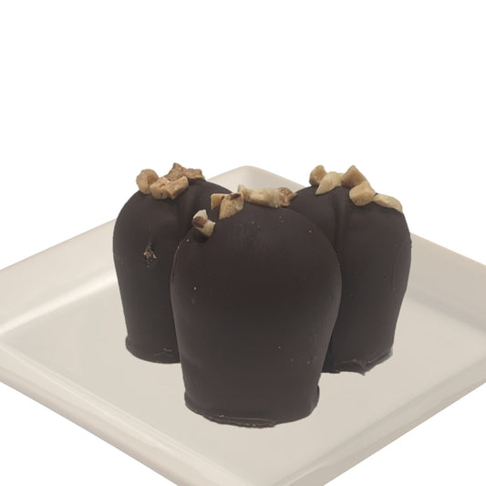 Four dark chocolate truffles with peanut topping on a white plate and white background