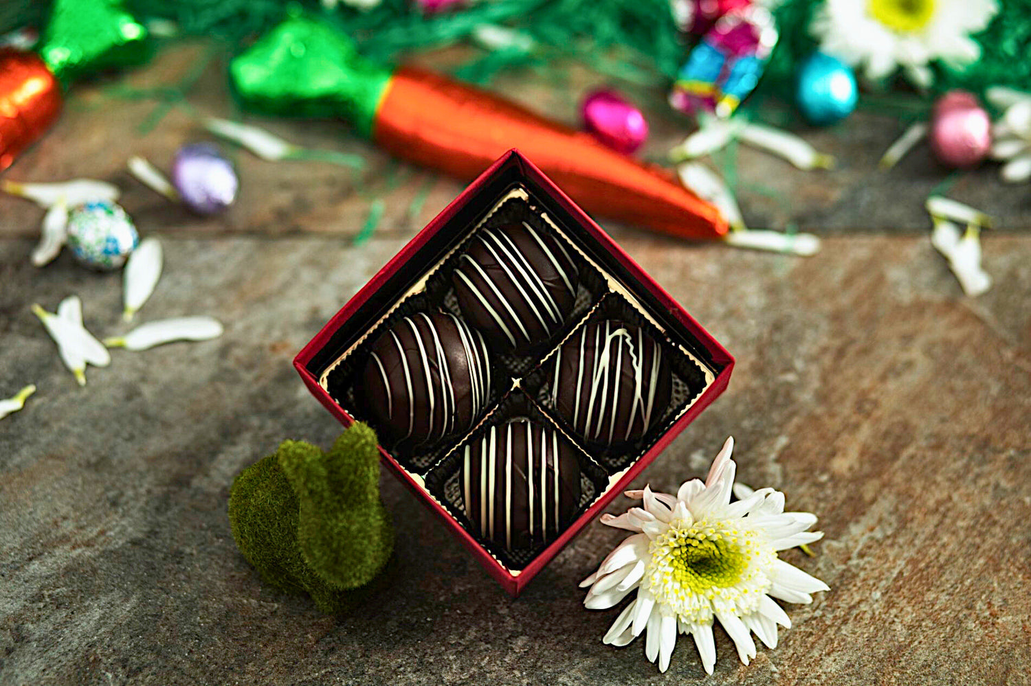 Open box of dark chocolates on a rustic stone surface with decorative elements.