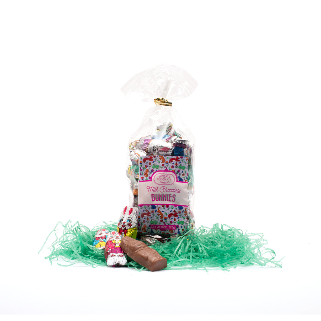 A clear plastic gift bag containing small foil-covered milk chocolate bunnies, with a pink Euphoria Chocolate Company label and ribbon decorations, presented on green decorative grass in front of a white background.