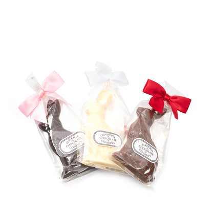 Three chocolate rabbits packaged in clear plastic, with decorative bows in pink and red. From left to right: white chocolate, milk chocolate, dark chocolate, all with the Euphoria Chocolate Company logo against a white background.