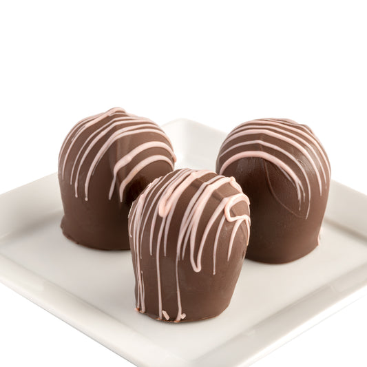 Three chocolate truffles with a stripe of pink chocolate on top, placed on a white plate in front of a white background.