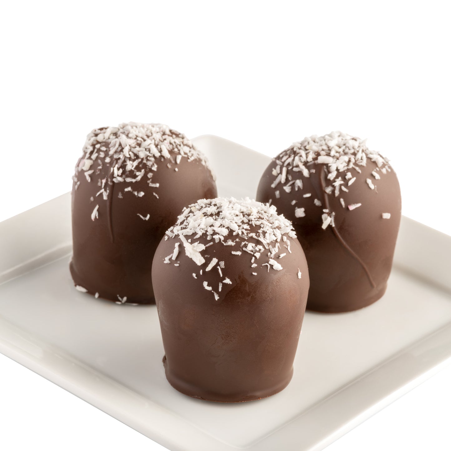 Three dark chocolate truffles with shredded coconut on top sitting on a white plate in front of a white background.