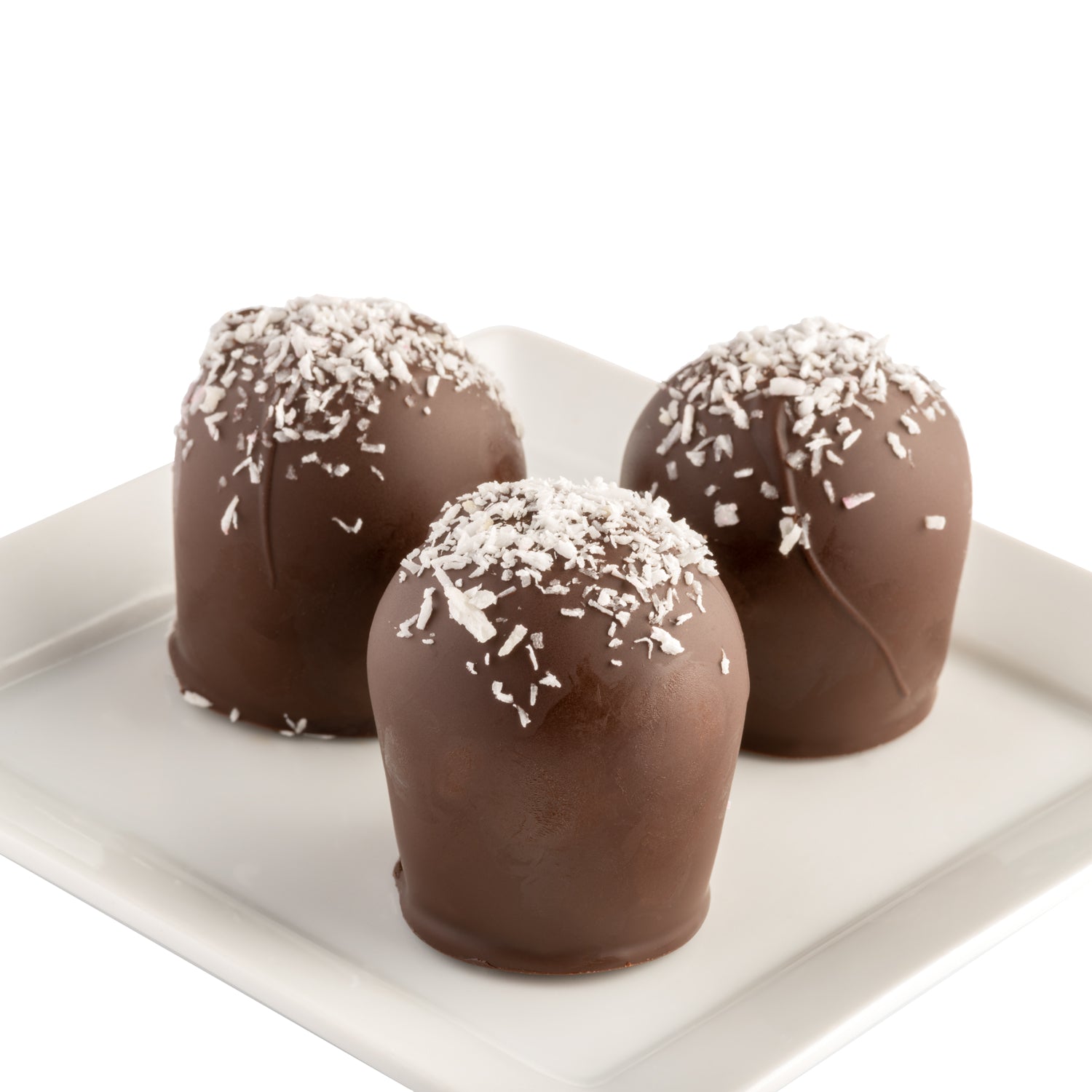 Three dark chocolate truffles with shredded coconut on top sitting on a white plate in front of a white background.