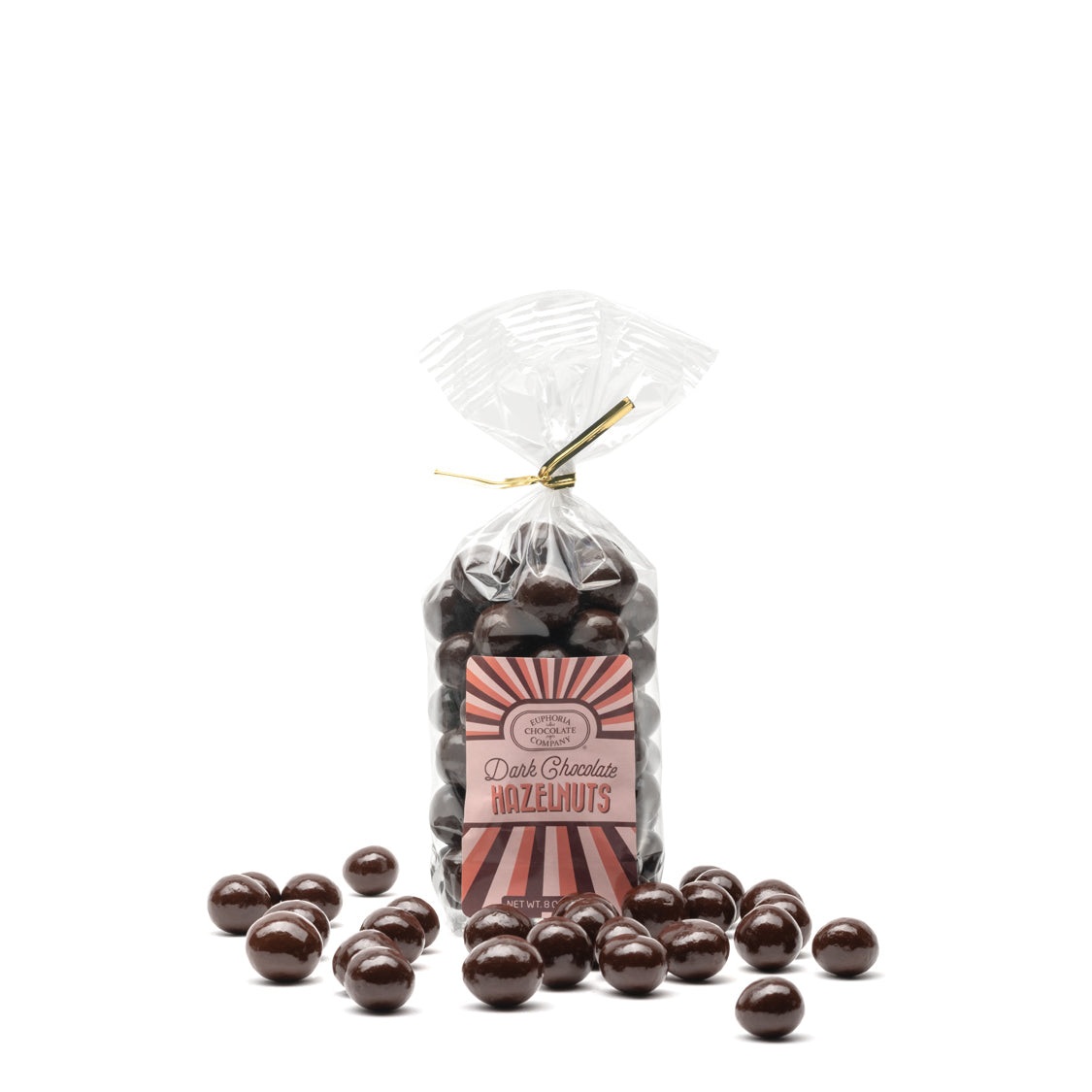 A clear plastic bag filled with dark chocolate covered hazelnuts, with a label showing the Euphoria Chocolate Company brand and the product name. A few chocolate-covered hazelnuts are scattered in front of the bag.