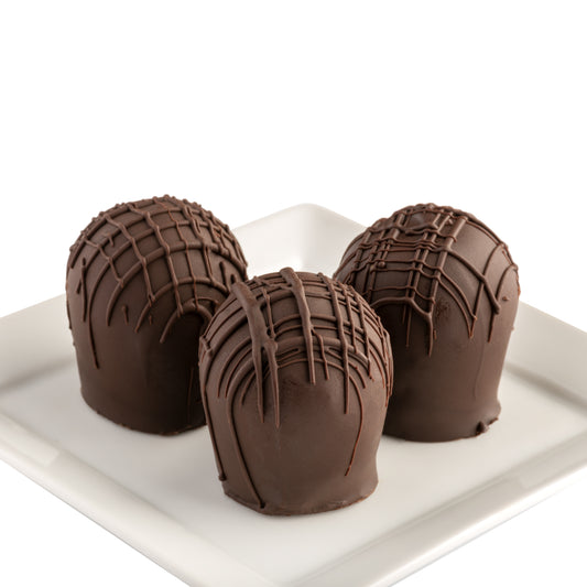 Three extra dark chocolate truffles with a textured design on the chocolate exterior, presented on a white plate against a white background.