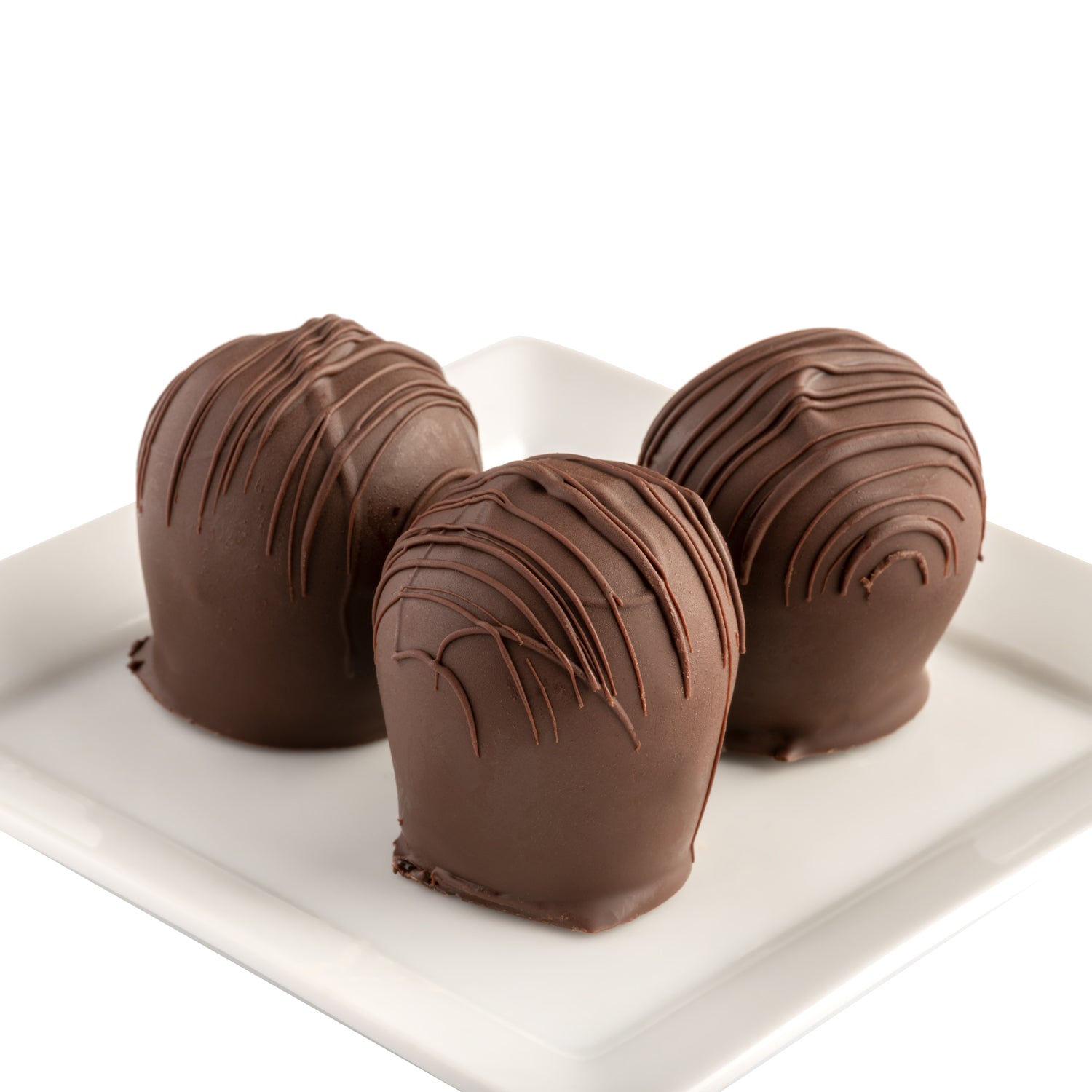 Three hand-dipped dark chocolate truffles with a dark chocolate drizzle on a white plate in front of a white background.