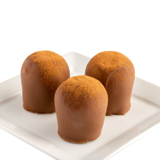 A set of three round chocolate truffles dusted with cinnamon, presented on a white plate in front of a white background.
