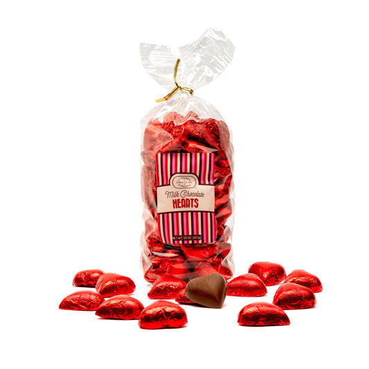 A clear plastic bag filled with red foil-wrapped heart-shaped milk chocolates, with a few chocolates scattered in front of the bag.