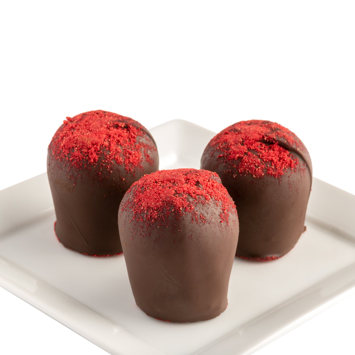 Three chocolate raspberry truffles with the topmost layer dusted in red powdered raspberry confection powder, presented on a white plate in front of a white background.