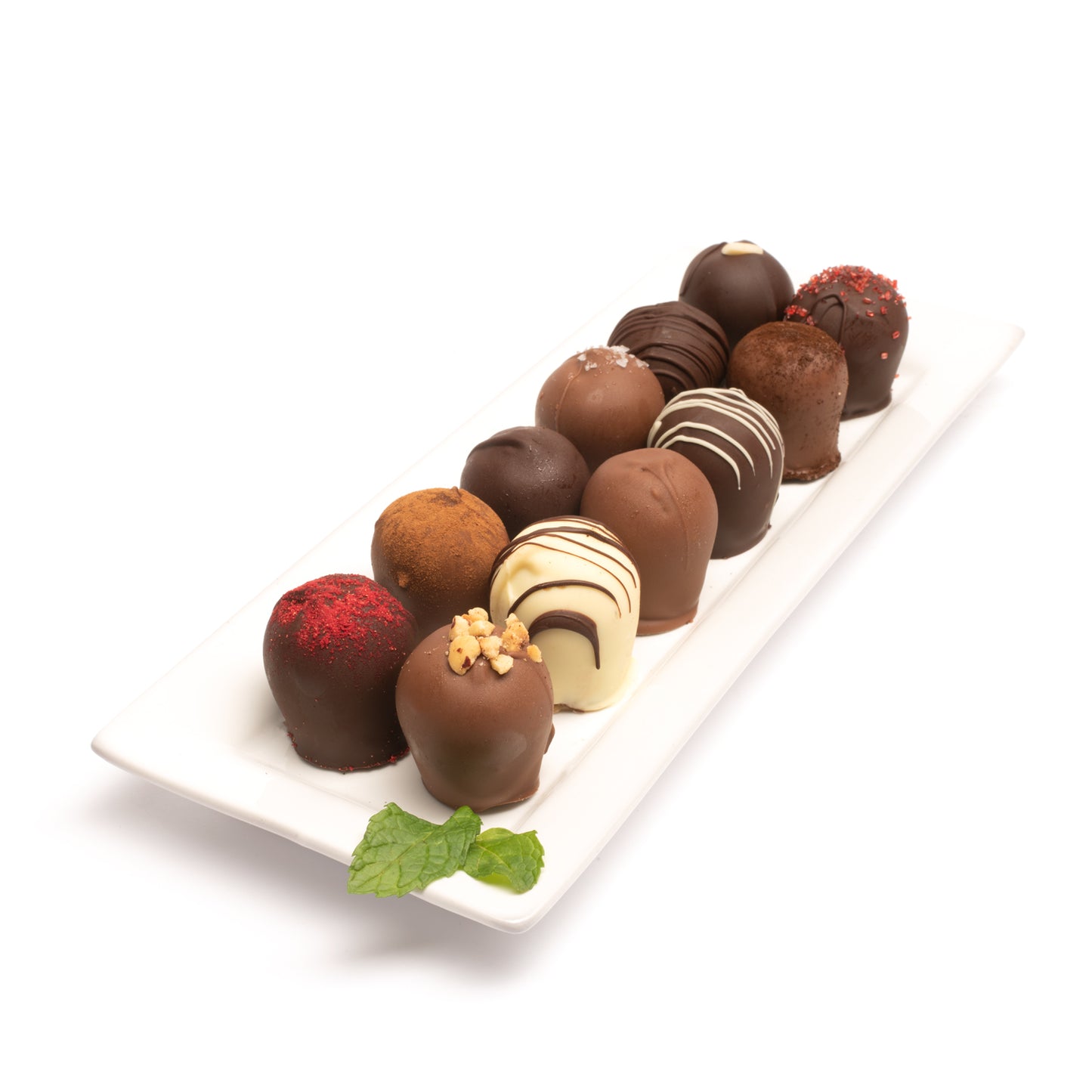 An assortment of 12 chocolate truffles on a white plate with a mint leaf in front of a white background.