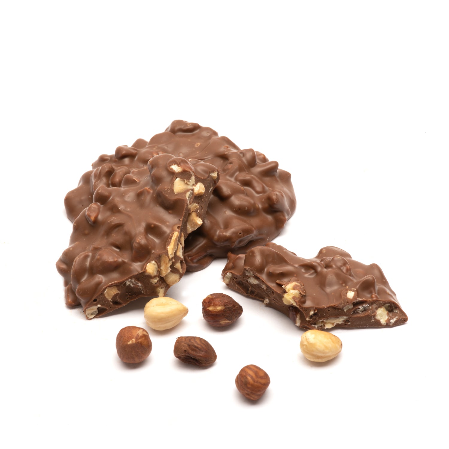 Pieces of milk chocolate nut clusters with visible hazelnuts inside with additional hazelnuts scattered around on a white background.