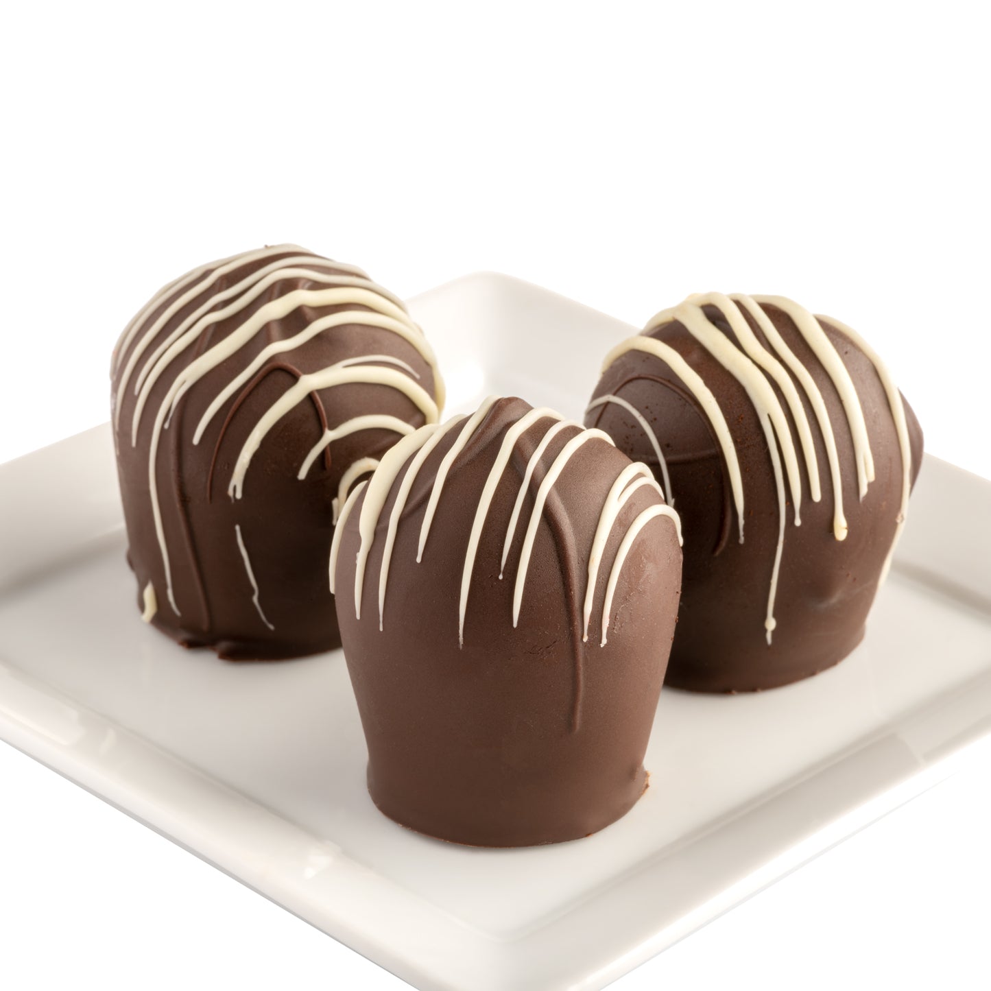 Three chocolate mint truffles with a dark chocolate coating and white chocolate drizzle on a white plate in front of a white background.