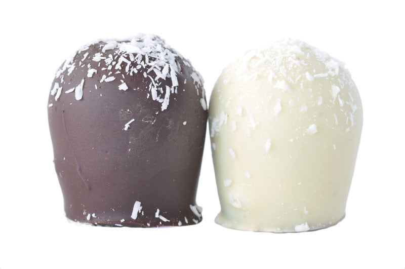 A closeup of two truffles, one dark chocolate and one white. Both truffles have shredded coconut flakes on top and are displayed in front of a white background.