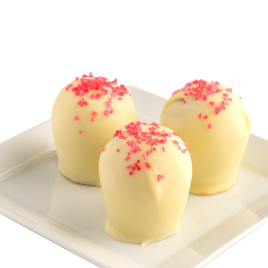 Three white chocolate truffles with red sugar crystals on top, presented on a white plate against a white background.